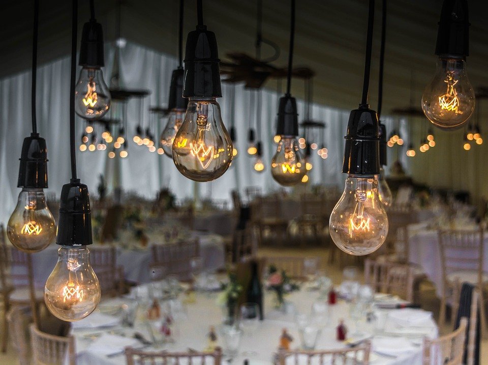 wedding-1937022_960_720.jpg Edison bulbs hang above elegantly set tables, casting a warm glow over a beautifully arranged wedding venue in Essex, thoughtfully prepared by a skilled wedding planner.